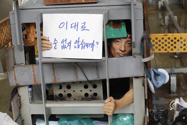 유최안 금속노조 거제통영고성조선하청지회 당시 부지회장 지난 2022년 6월24일 오후 경남 거제 대우조선해양 1 도크 선박에서 1㎥ 케이지를 만들고 들어가 끝장 농성을 벌이고 있는 모습. 유 전 부지회장은 ‘이대로 살 순 없지 않겠습니까?’라고 쓴 손팻말을 들어 보이고 있다. 사진=금속노조